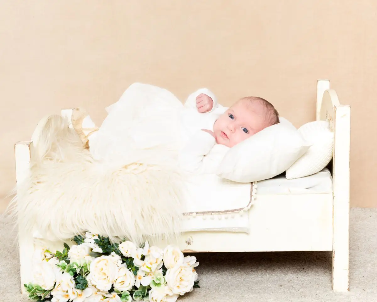 a tiny baby laying on a miniature white bed at a professional portrait shoot