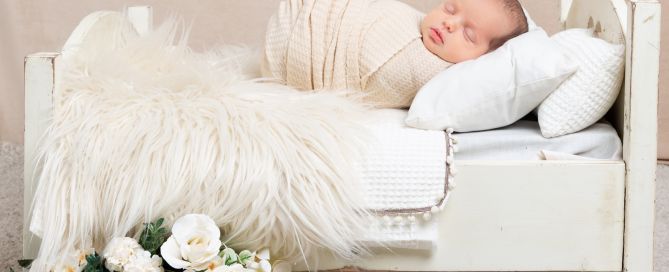 a sleeping newborn wrapped in cream on a miniature bed with flower decorations