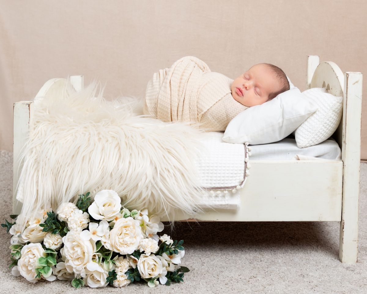 a sleeping newborn wrapped in cream on a miniature bed with flower decorations