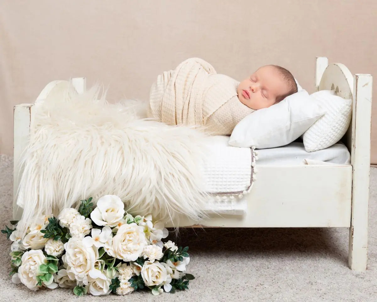 a sleeping newborn wrapped in cream on a miniature bed with flower decorations