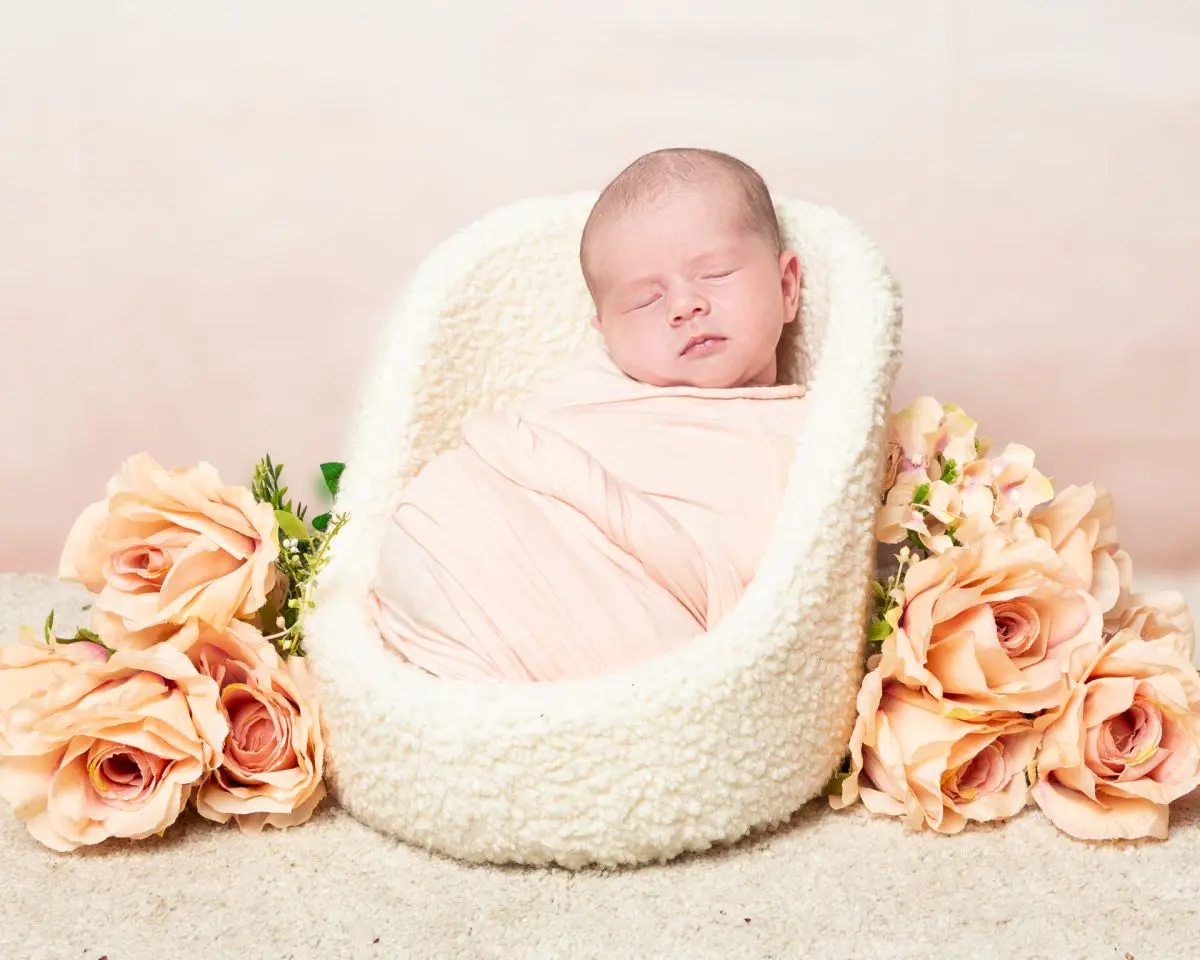 a little girl swaddled in peach sleeps in a chair next to peach flowers