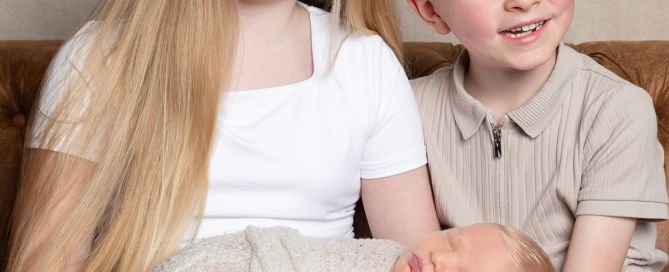 a brother and sister hold their newborn sibling at a professional photo shoot.