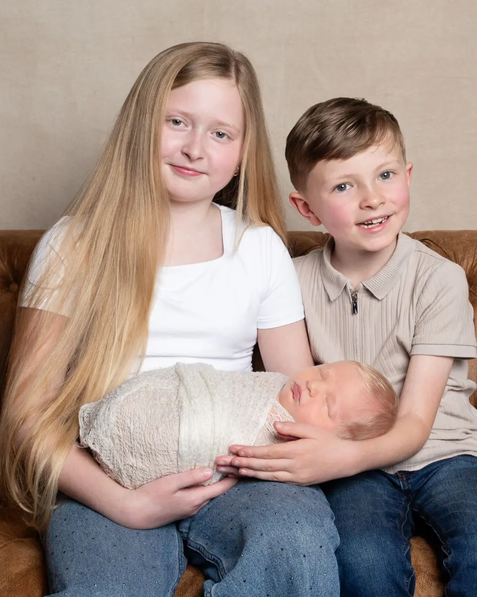 a brother and sister hold their newborn sibling at a professional photo shoot.