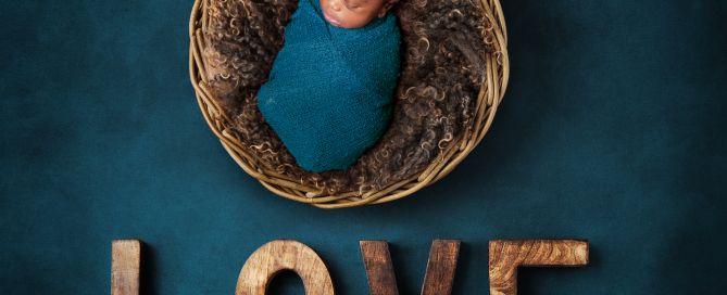 A baby swaddled in teal is photographed in a newborn photo shoot