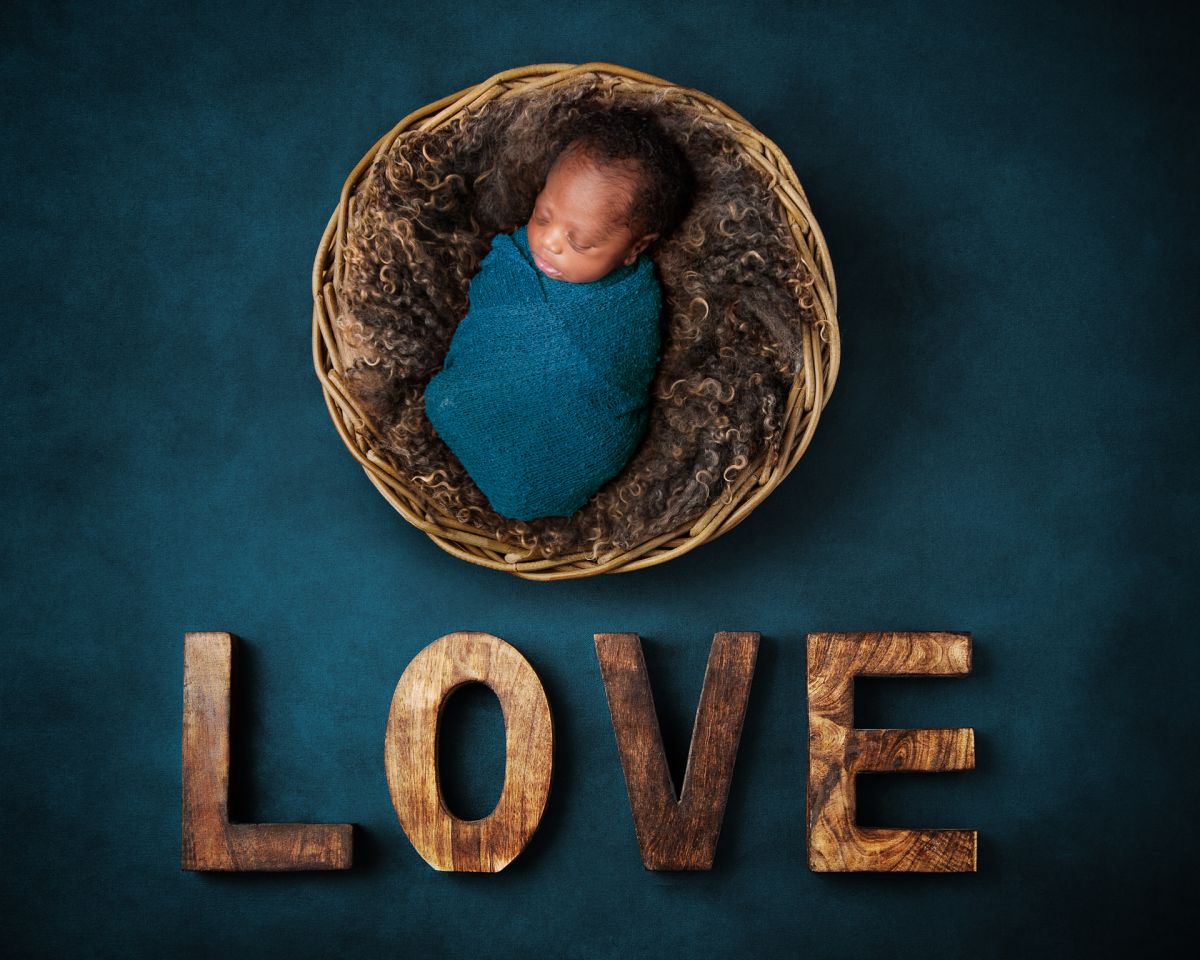 A baby swaddled in teal is photographed in a newborn photo shoot