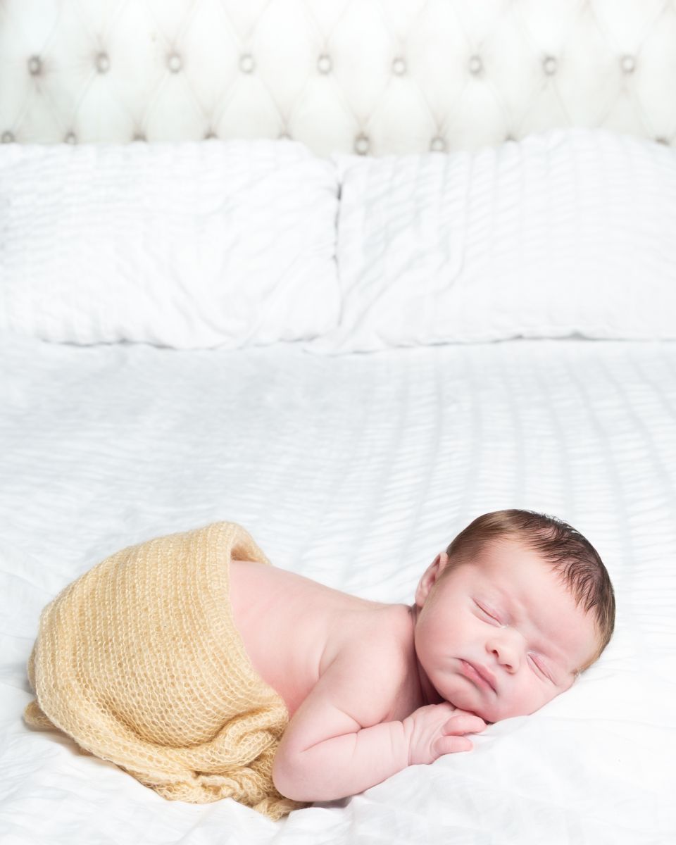 a newborn part swaddled sleeps on a bed at a photo shoot
