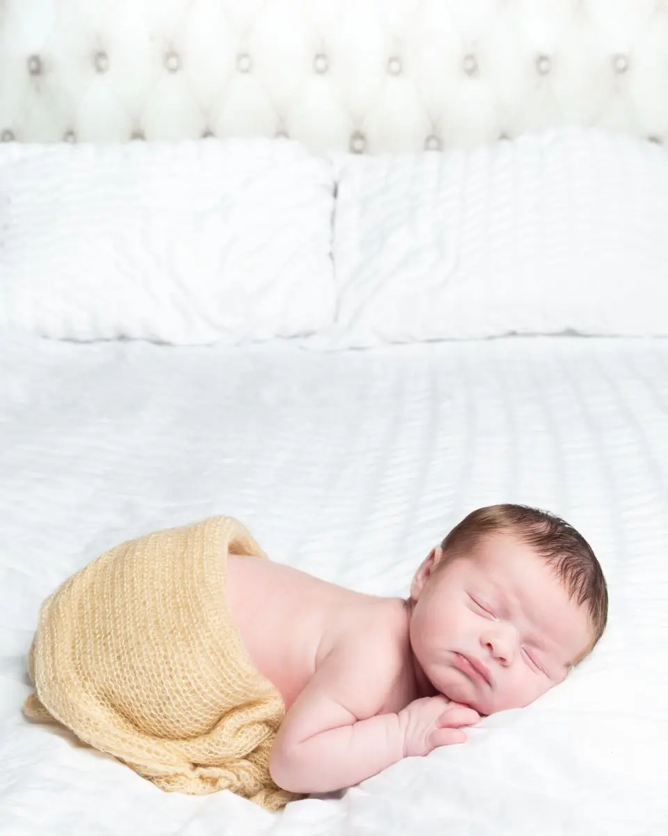 a newborn part swaddled sleeps on a bed at a photo shoot