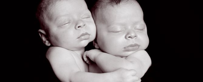 twin newborns cuddled together against a black backdrop