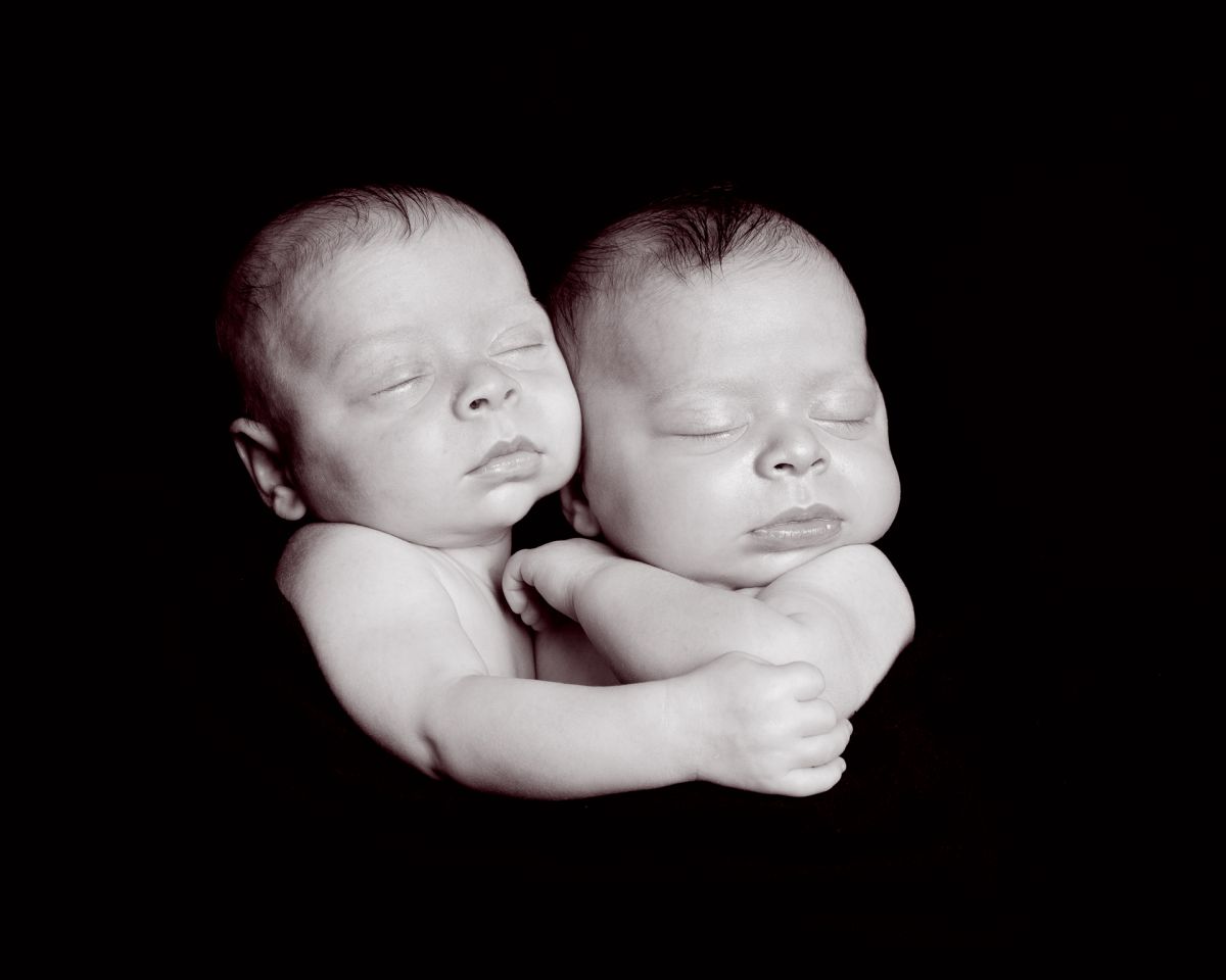 twin newborns cuddled together against a black backdrop