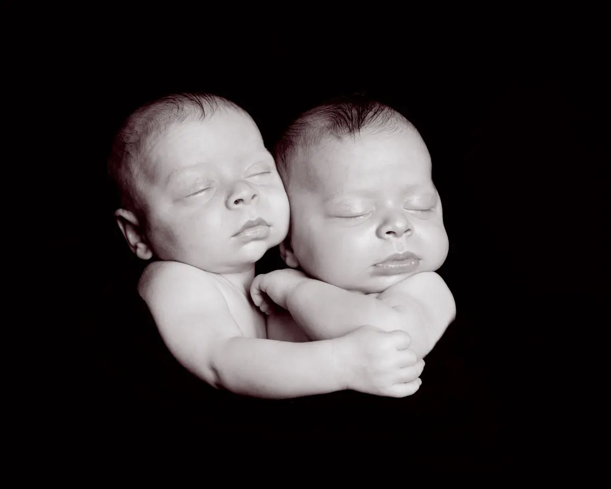 twin newborns cuddled together against a black backdrop