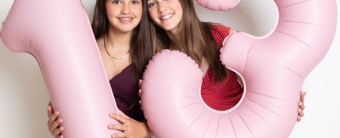 two girls pose with balloons shaped like the number 13 to celebrate their birthdays