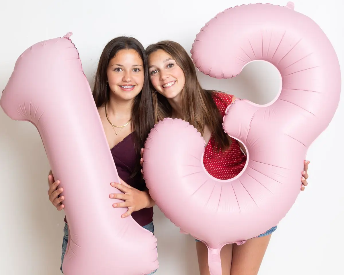 two girls pose with balloons shaped like the number 13 to celebrate their birthdays