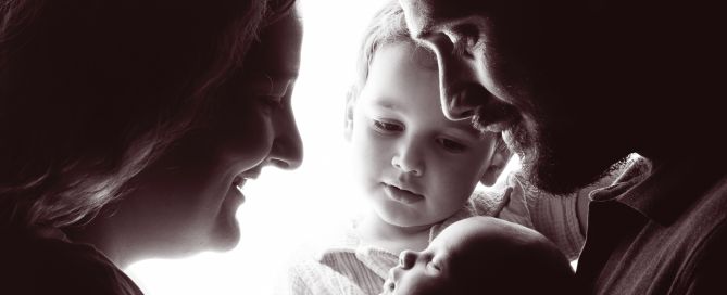 A family of four gathered in a silhouette image looking at their newborn family member