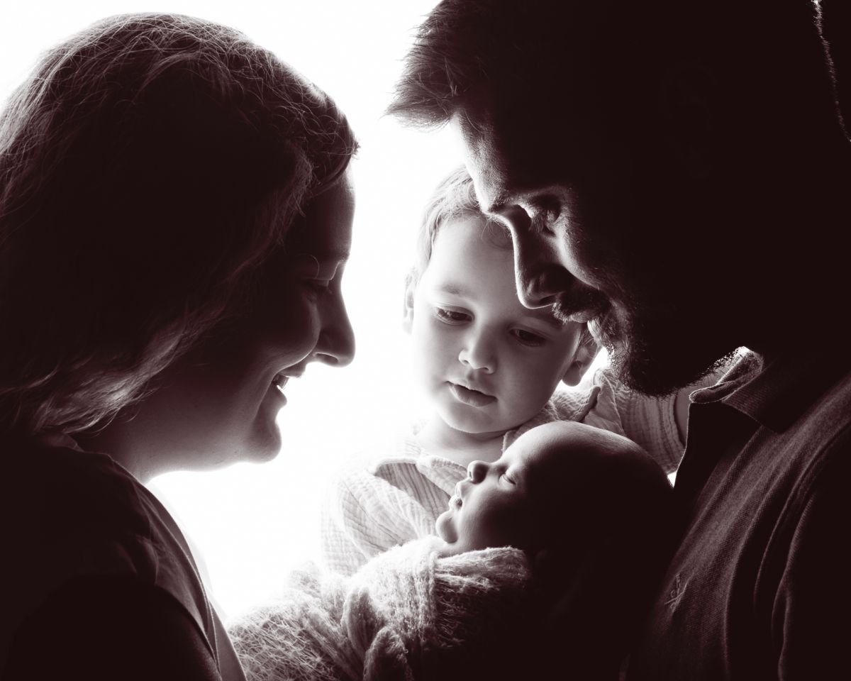 A family of four gathered in a silhouette image looking at their newborn family member