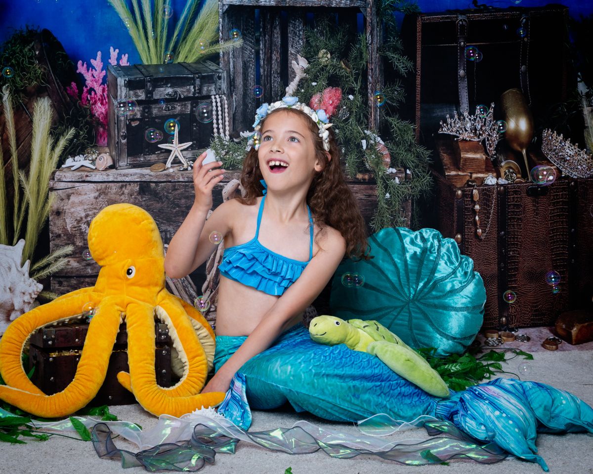 a little girl dressed as a mermaid is excited when the bubble machine is turned on