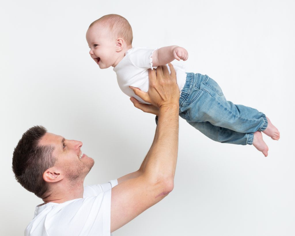 a baby is flown up in the air by their dad at a portarit session