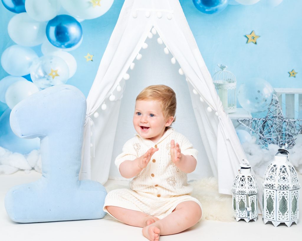 a little boy claps his hand against a blue starry backdrop at a first birthday photo shoot