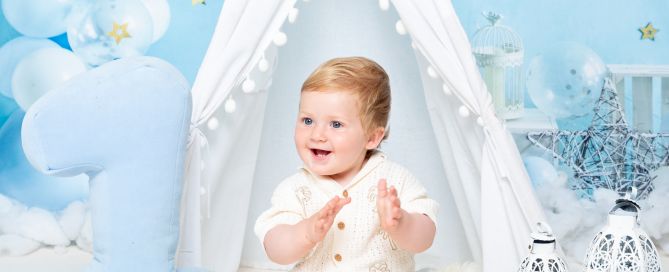 a little boy claps his hand against a blue starry backdrop at a first birthday photo shoot