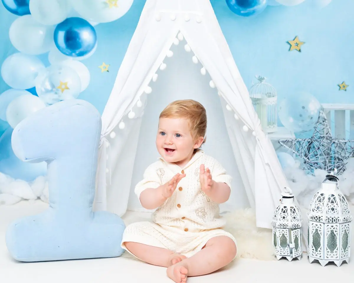 a little boy claps his hand against a blue starry backdrop at a first birthday photo shoot