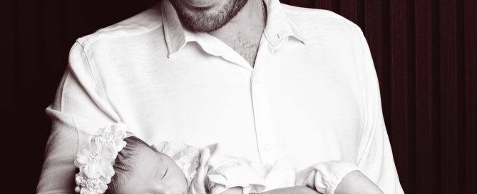 A dad cradles his newborn daughter against a black background at a photo shoot