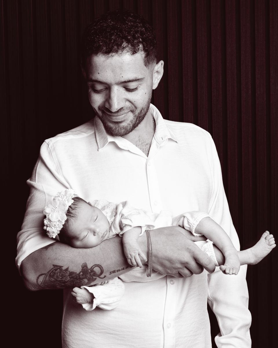 A dad cradles his newborn daughter against a black background at a photo shoot
