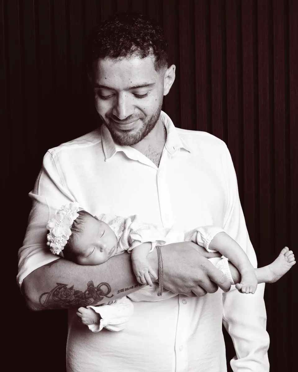 A dad cradles his newborn daughter against a black background at a photo shoot