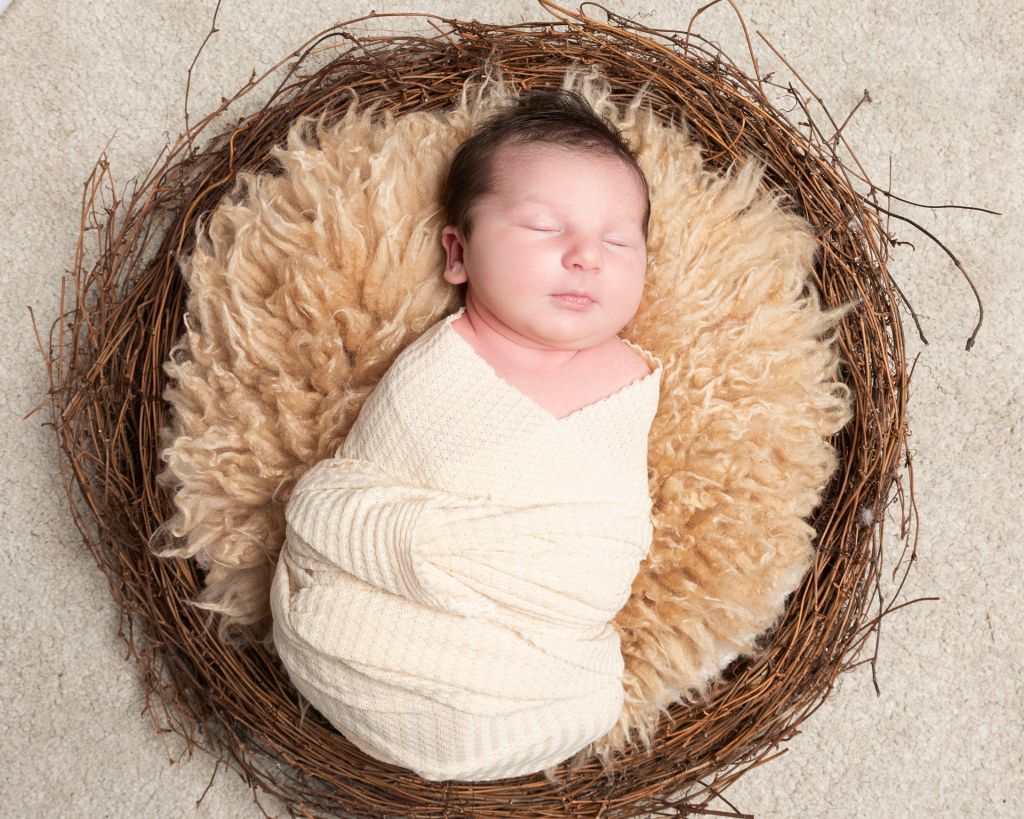 a baby sleeps swaddled in a nest with a beige fluffy blanket