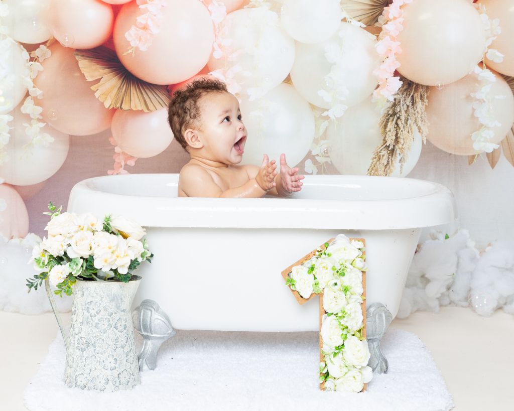 a little girl playing in bubbles and splashing in a tub at a first birthday photo shoot