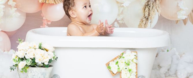 a little girl playing in bubbles and splashing in a tub at a first birthday photo shoot