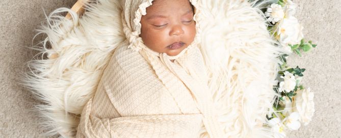 a newborn baby in a cream wrap and bonnet in a floral cream themed photo shoot
