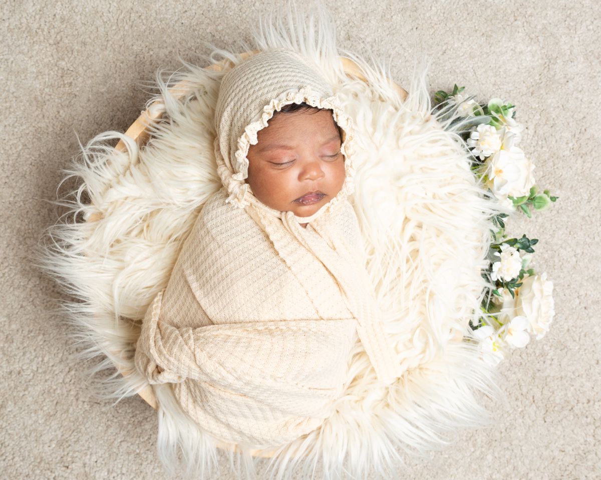 a newborn baby in a cream wrap and bonnet in a floral cream themed photo shoot