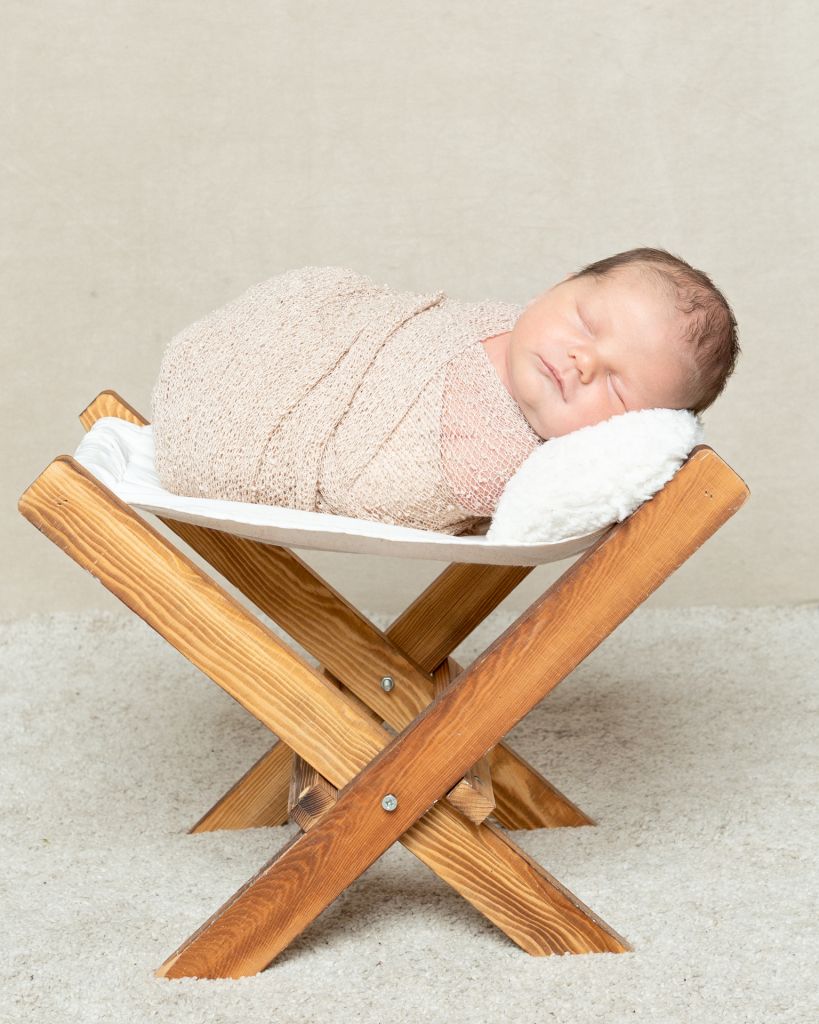 a little boy in a beige wrap on a little wooden hammock