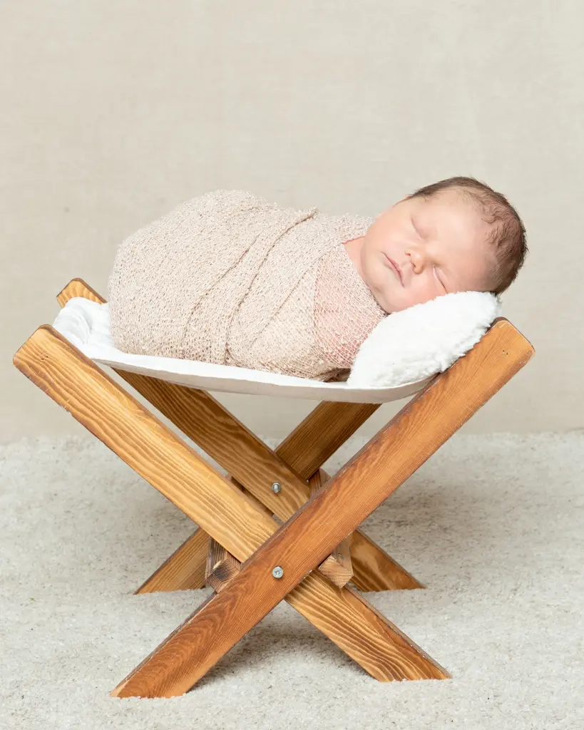 a little boy in a beige wrap on a little wooden hammock