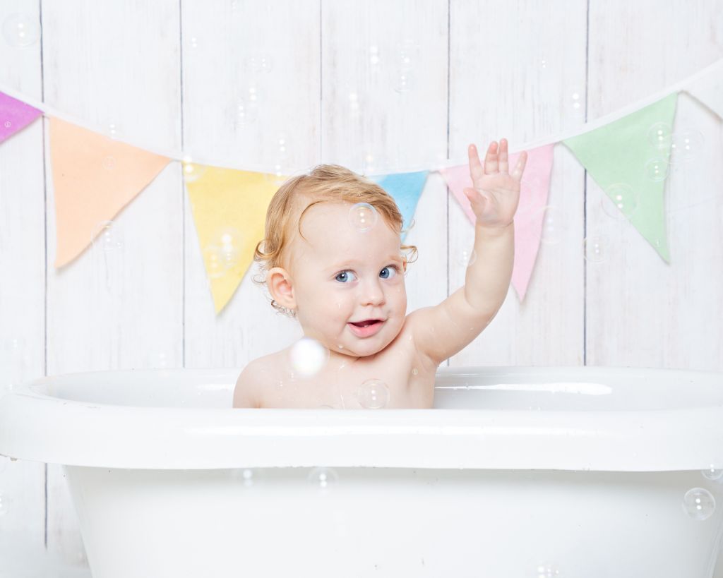 a baby waving in a tub surrounded by bubbles at a photo shoot