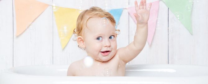 a baby waving in a tub surrounded by bubbles at a photo shoot