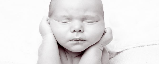 a black and white image of a newborn baby in a traditional froggy pose at a newborn photo shoot