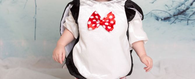 a baby dressed as a penguin in front of a snow scene in a photographic studio
