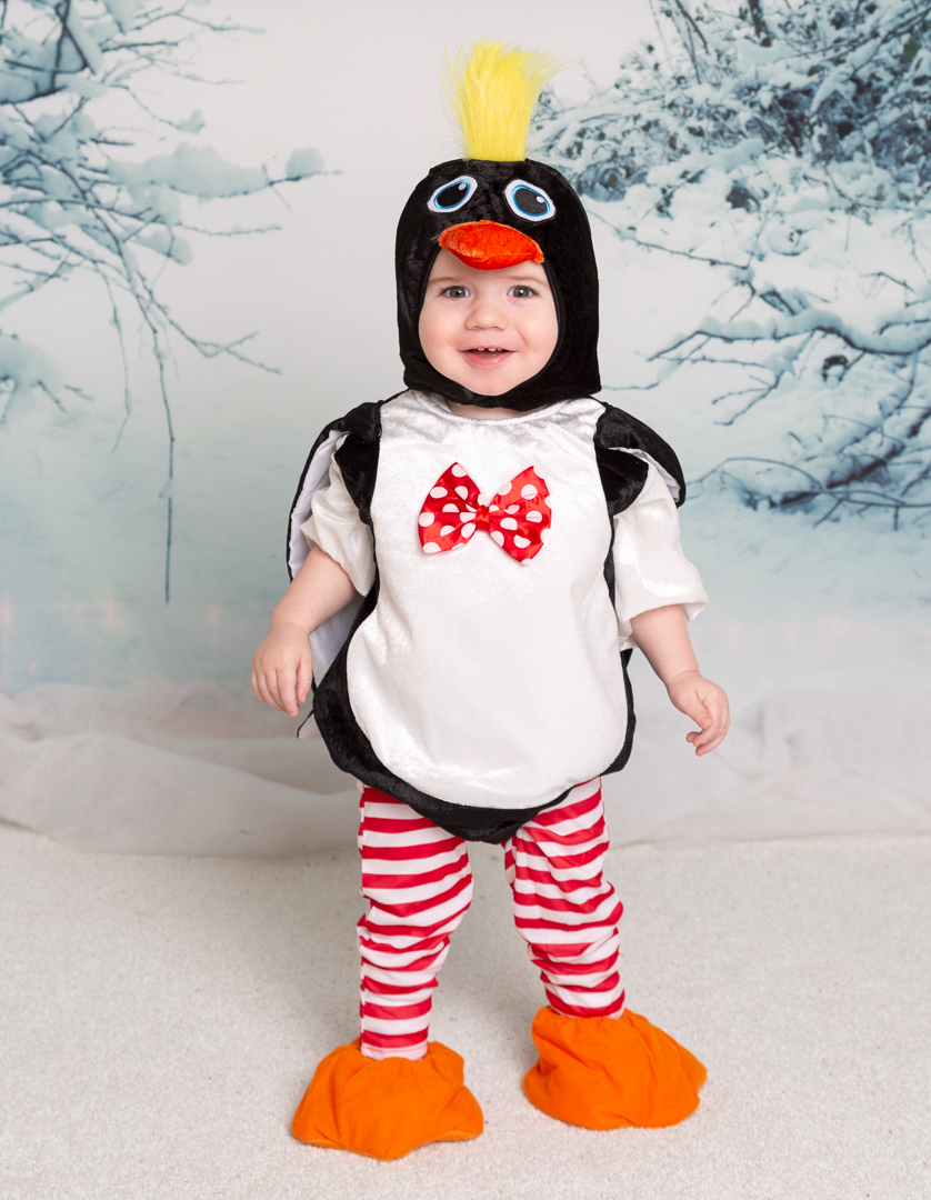 a baby dressed as a penguin in front of a snow scene in a photographic studio