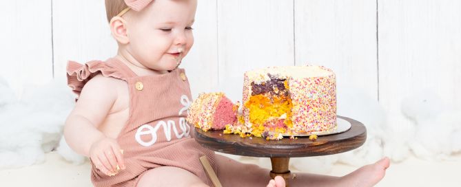 a little girl in a pink romper with a rainbow cake