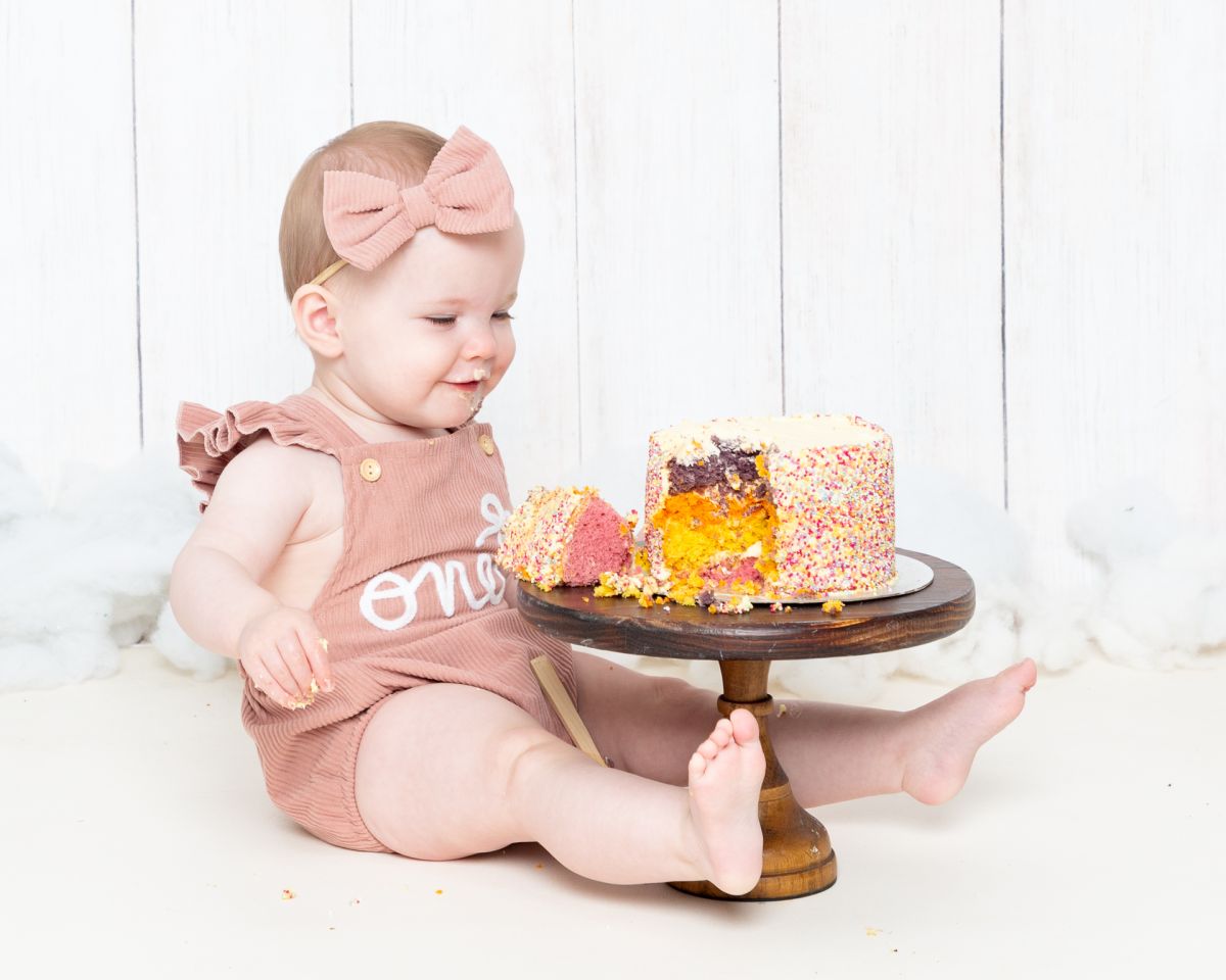 a little girl in a pink romper with a rainbow cake