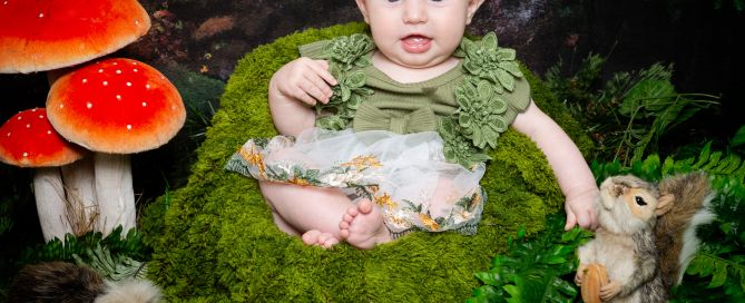 a baby girl sits in a moss covered chair in a woodland themed photo shoot