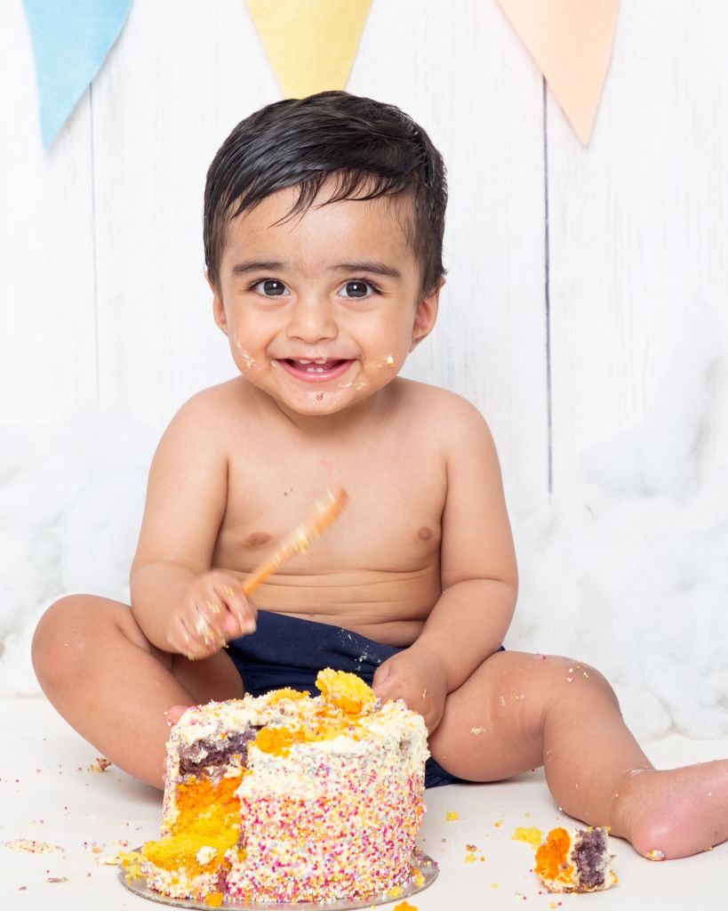 a little boy holding a spoon at his cake smash photo shoot
