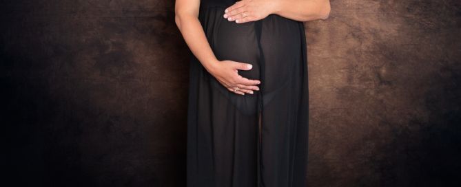 a pregnant lady in a black dress in front of a fine art brown backdrop