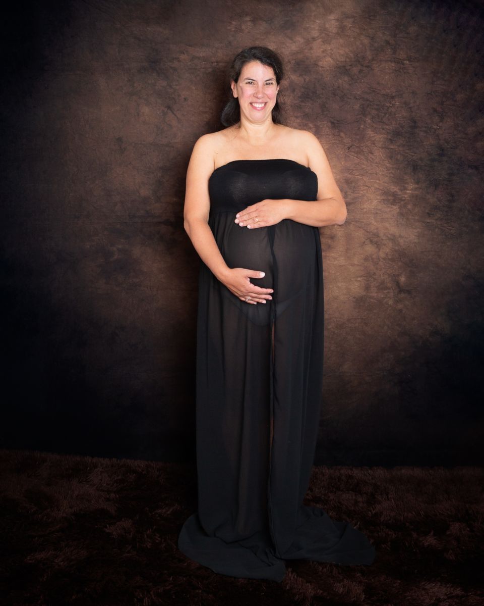 a pregnant lady in a black dress in front of a fine art brown backdrop