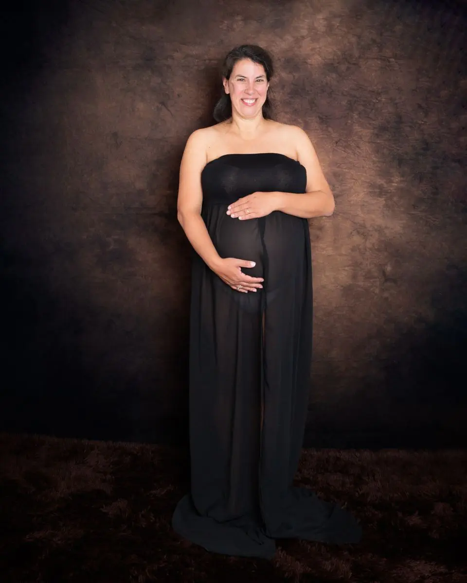 a pregnant lady in a black dress in front of a fine art brown backdrop